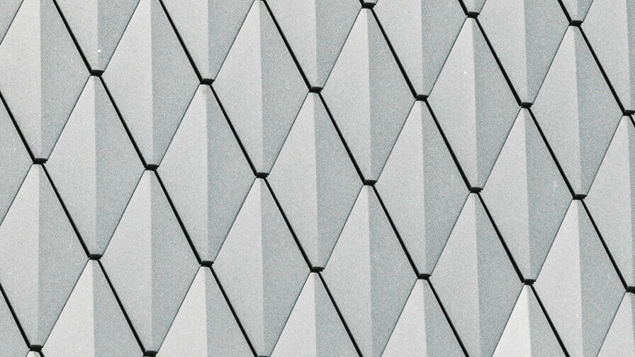 Trapézová vikierová strecha rodinného domu v Mechernichu, obložená malými strešnými šablónami PREFA v odtieni P.10 antracitová. Strecha je pokrytá strešnými šindľami PREFA DS.19 v rovnakom odtieni. Vysoko kvalitný hliníkový obklad zaisťuje odolnosť voči poveternostným vplyvom a moderný, estetický vzhľad.