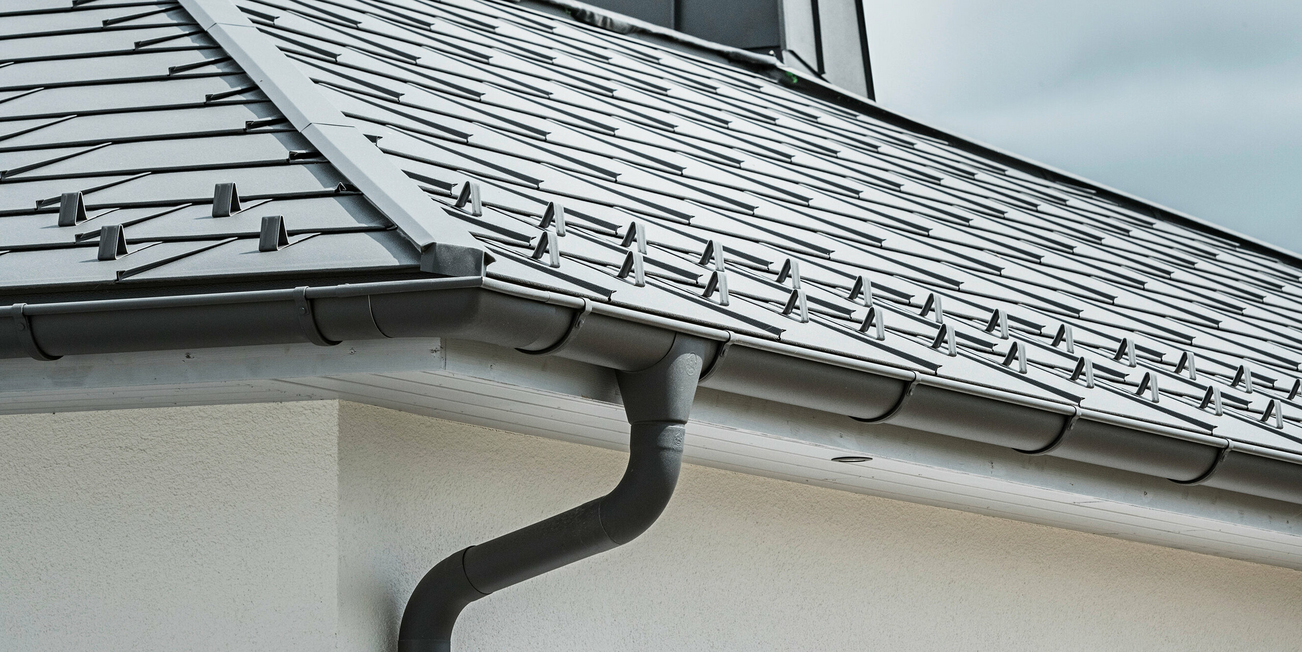 Strešný panel PREFA R.16 a PREFALZ ako aj dažďový zvod a polkruhový žľab P.10 tmavošedá na streche bungalovu