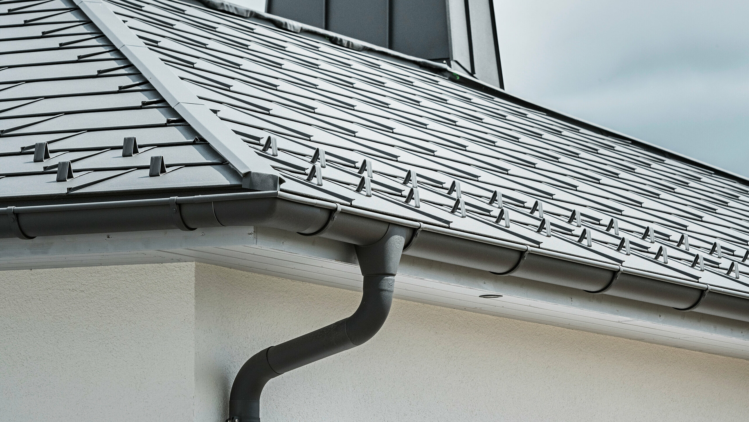 Strešný panel PREFA R.16 a PREFALZ ako aj dažďový zvod a polkruhový žľab P.10 tmavošedá na streche bungalovu