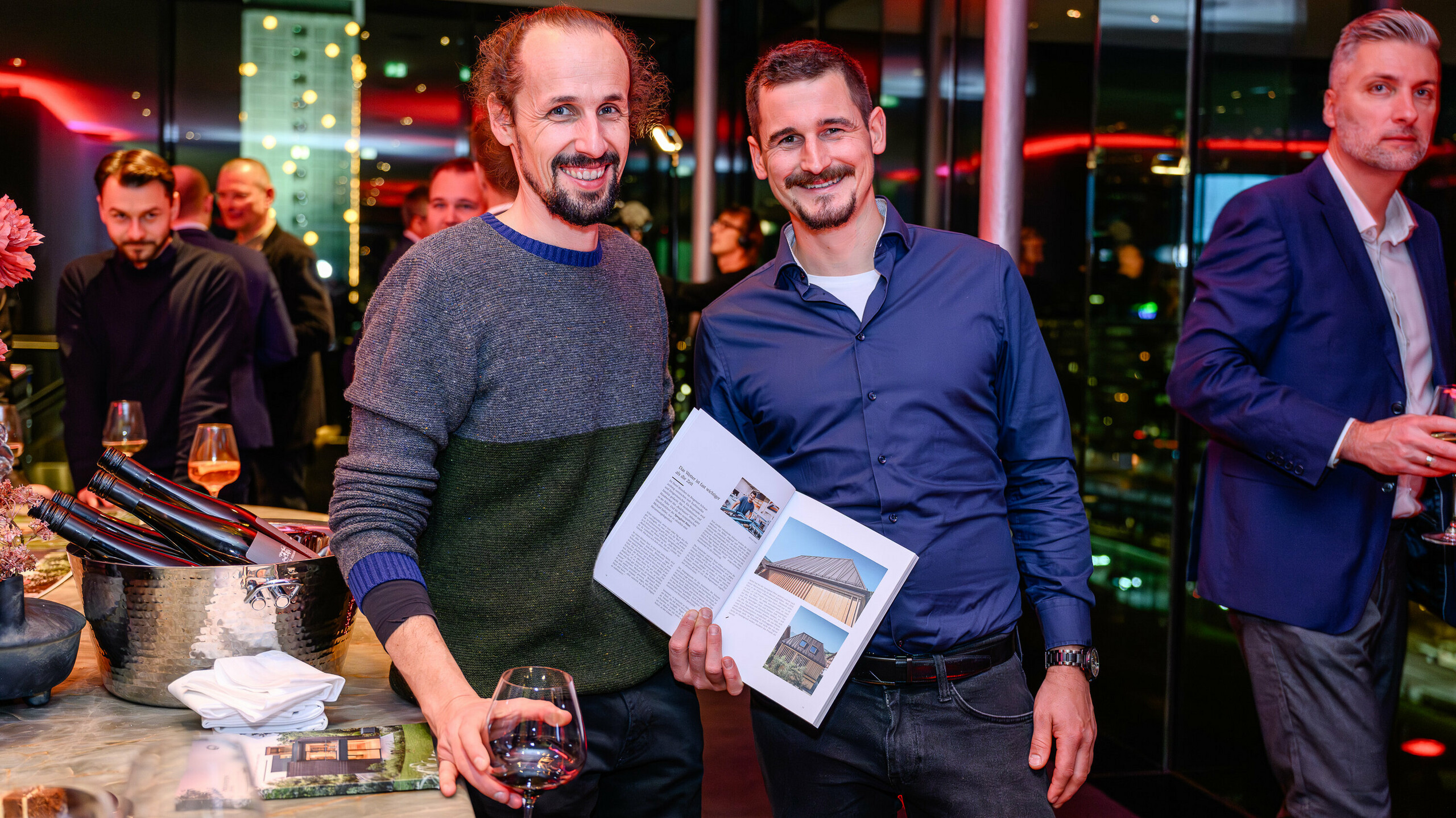 Žiarivé tváre na prezentácii PREFARENZEN 2026: Dvaja účastníci projektu hrdo prezentujú svoj publikovaný objekt v novej knihe o architektúre PREFA. Na obrázku je vila, ktorá kombinuje prírodný vzhľad dreva s PREFALZ – vynikajúci príklad moderného kontrastu materiálov a trvalej estetiky. Podujatie v k47.wien spája dizajn, architektúru a networking na najvyššej úrovni. Hliníkové produkty PREFA tu ukazujú svoju plnú silu: odolnosť voči poveternostným vplyvom, kreatívne využitie a štýlovú tvorbu pre budúcnosť orientované stavebné projekty. Večer plný hrdosti, výmeny názorov a inovácií.