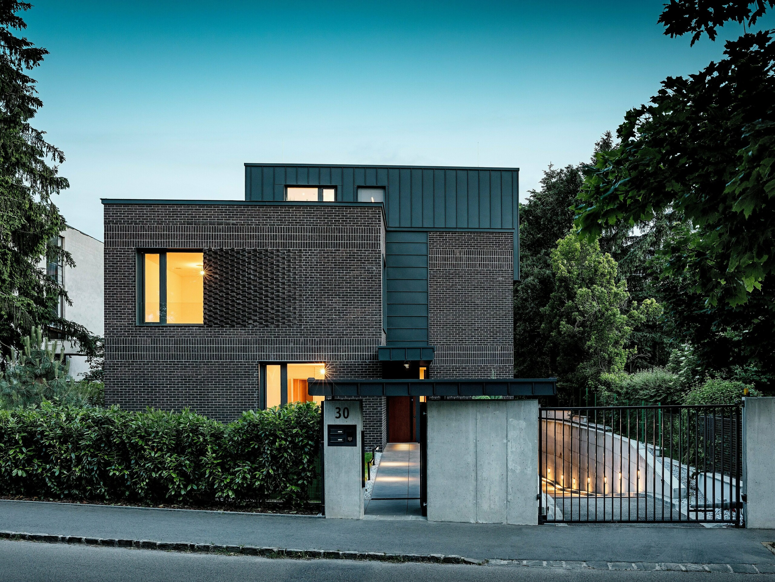 Na obrázku je moderný bytový dom v Budapešti, ktorého kubická strešná konštrukcia z hliníka PREFALZ v odtieni P.10 antracit vytvára výrazný kontrast s historickým okolím. Vertikálne uhlové stojaté falce vytvárajú zaujímavú hru svetla a zdôrazňujú jasný architektonický jazyk. Vysoko kvalitné hliníkové produkty PREFA dodávajú budove nielen elegantný, nadčasový vzhľad, ale presviedčajú aj svojou dlhou životnosťou, odolnosťou voči poveternostným vplyvom a precíznou spracovanosťou. Antracitová farba fasády a strechy pôsobí ako silný magnet pre pohľad a podčiarkuje inovatívny charakter stavby.