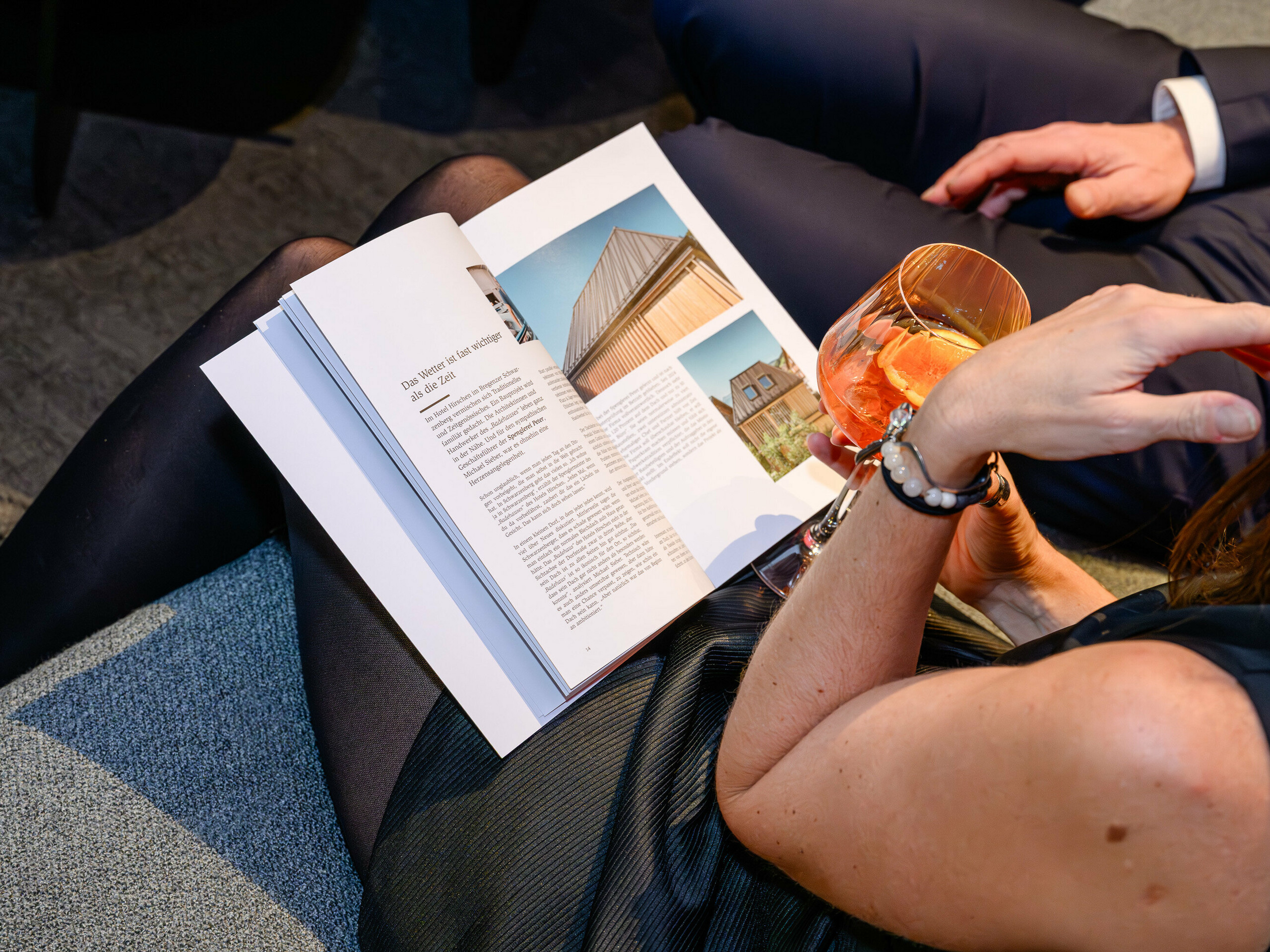 Atmosférická scéna na prezentácii PREFARENZEN 2026 v k47.wien: Elegantná žena s drinkom v ruke listuje v novej knihe o architektúre PREFA – pútavom diele plnom inšpiratívnych návrhov. Viditeľný je objekt s PREFALZ, ktorý zaujme moderným charakterom hliníka. Obrázok vyjadruje potešenie, výmenu a zvedavosť na inovácie. Vysoko kvalitný povrch PREFA spája estetiku a dlhú životnosť – ideálny pre kreatívne architektonické nápady. Hliník od PREFA stanovuje štandardy a nadchýna profesionálov, ako sú projektanti, architekti a spracovatelia.