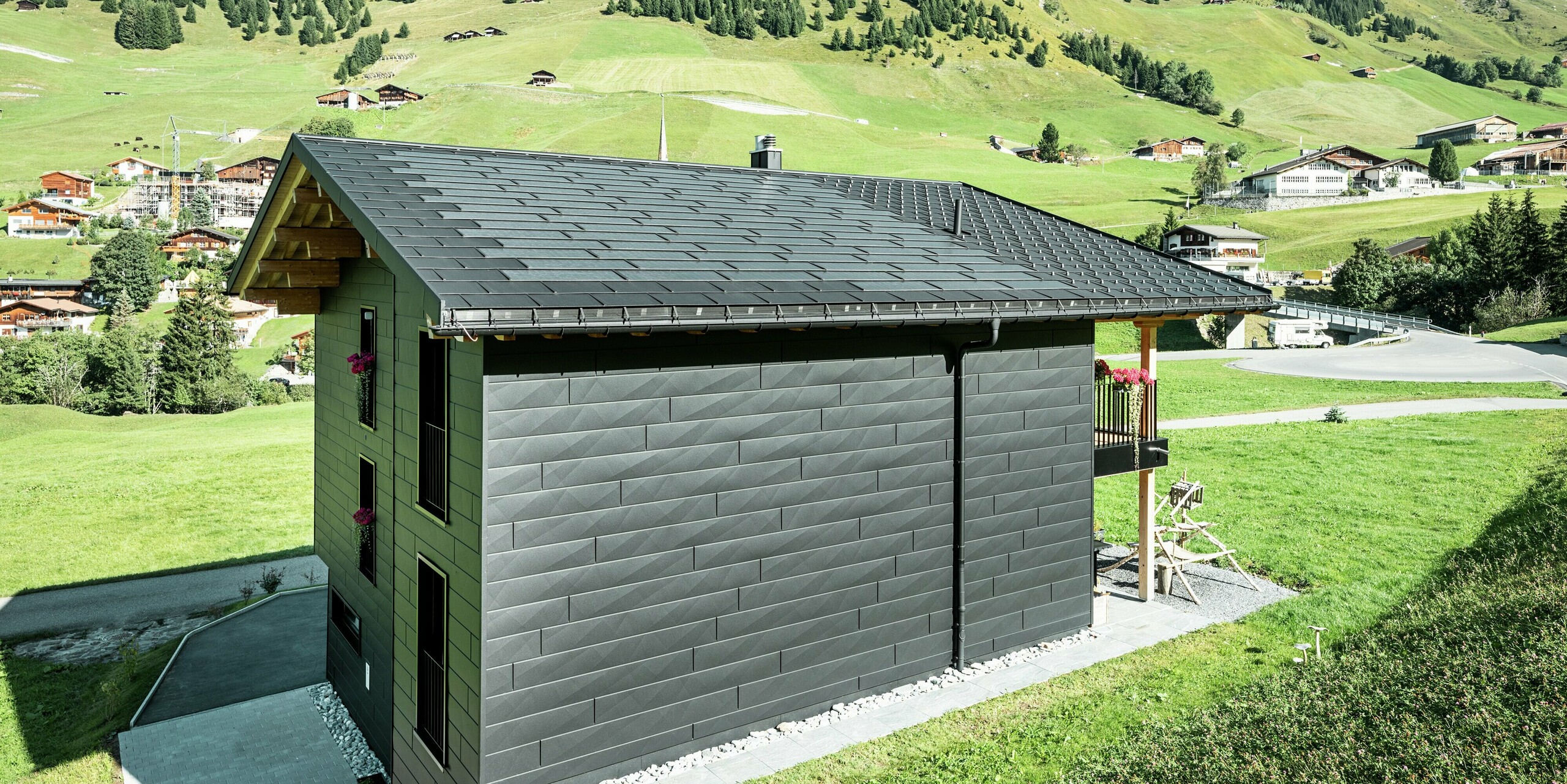 Bočný pohľad na rodinný dom s jasným výhľadom na strešné a fasádne produkty PREFA z hliníka. Integrované strešné panely a strešné panely R.16 v čiernej farbe P.10 nielenže poskytujú ochranu pred poveternostnými vplyvmi, ale aj moderný, nezameniteľný vzhľad. PREFA odvodňovací žľab a zvod sú perfektne integrované a fasádne panely Siding.X dodávajú budove nezameniteľný charakter.