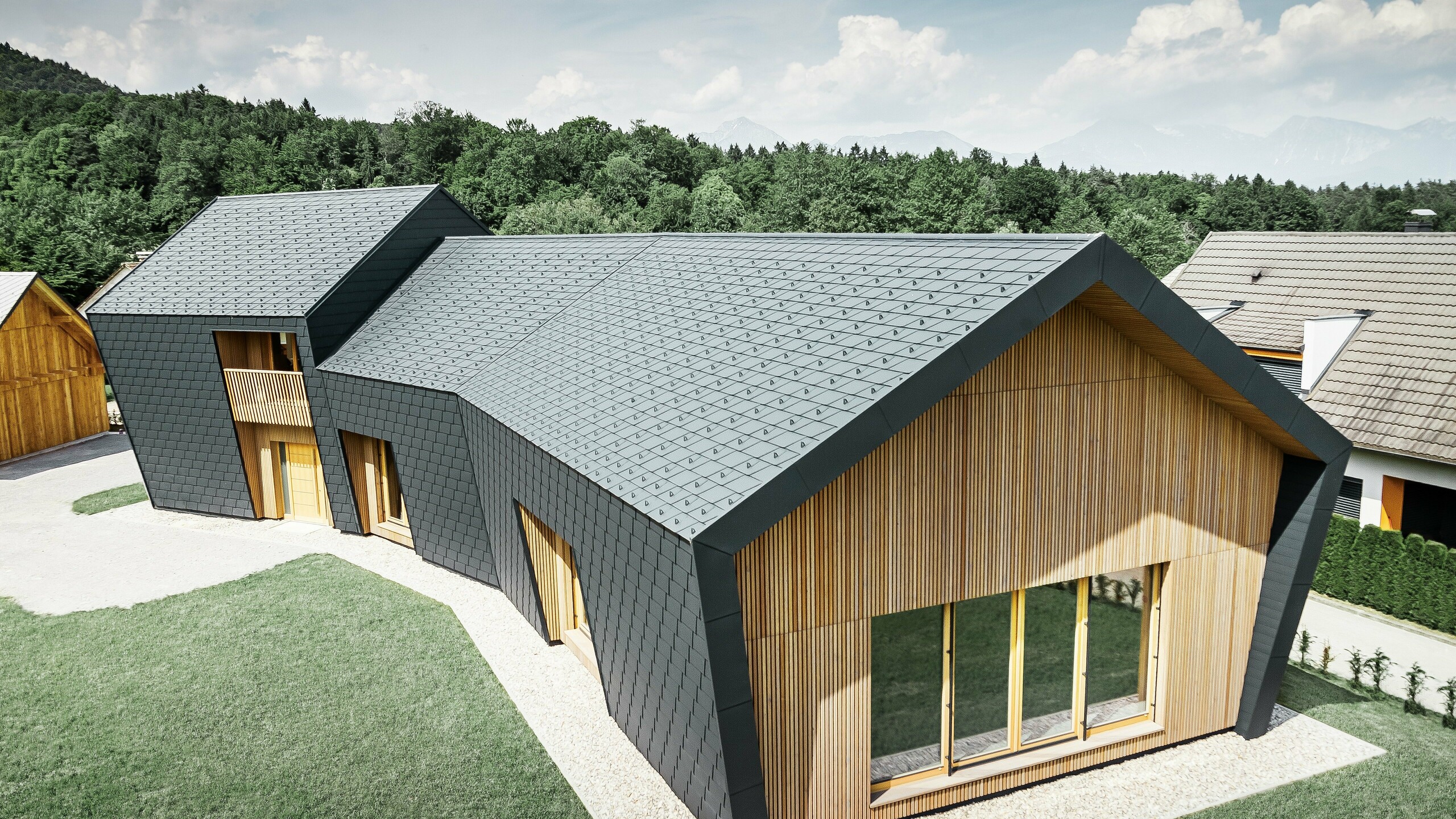 Veľké plochy na streche a fasáde pokryté strešným šindľom DS.19 vo farbe P.10 antracitová, na čelnej strane je fasáda obložená drevom