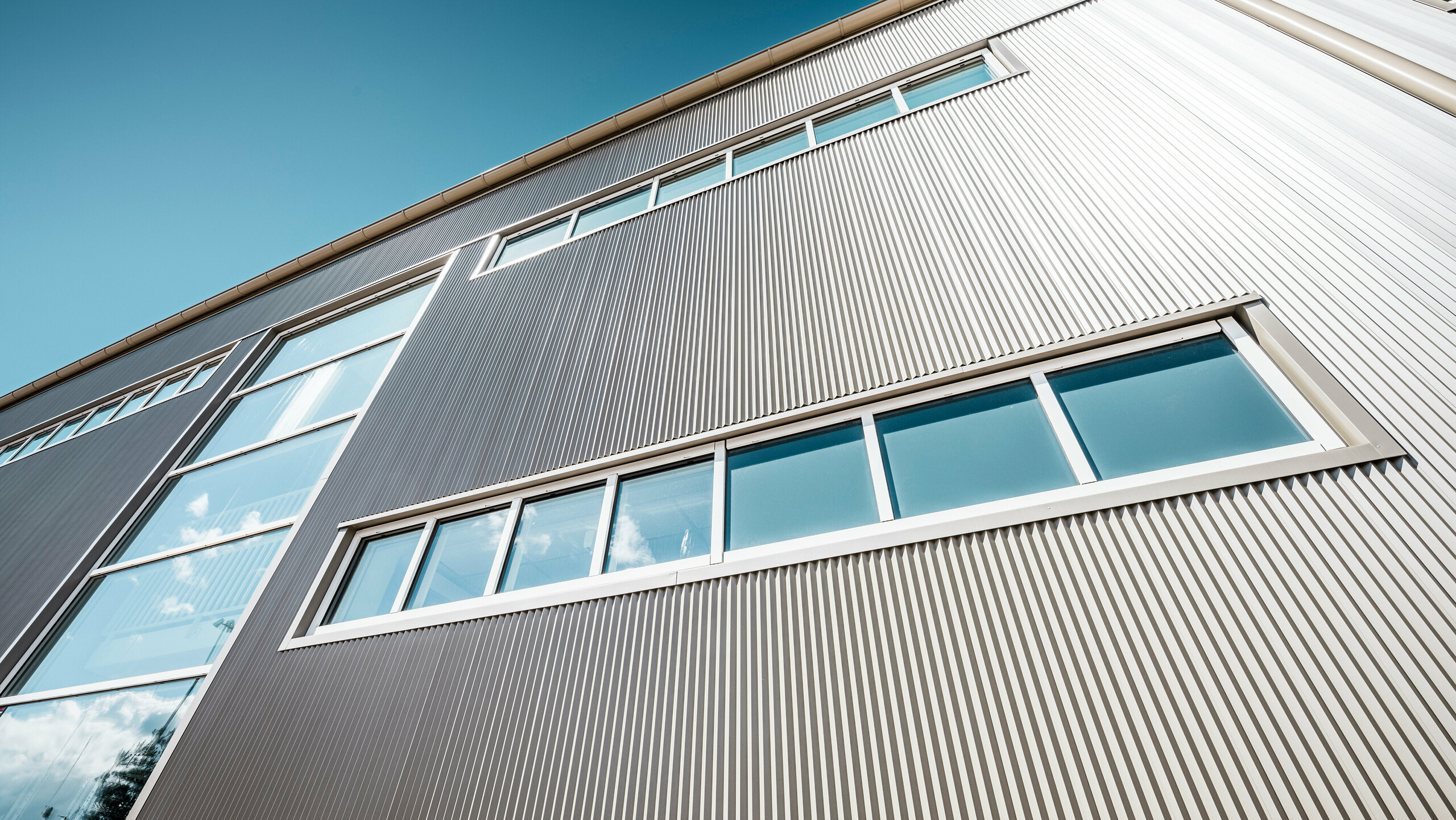 Pohľad na Park Arenu vo švédskom meste Värnamo s modernou bronzovou fasádou PREFA. Prelamované hliníkové profily vytvárajú pôsobivé efekty svetla a tieňa. Zabudované okná harmonicky zapadajú do precízne vyhotovenej fasády, ktorá je symbolom trvanlivosti, odolnosti a moderného dizajnu