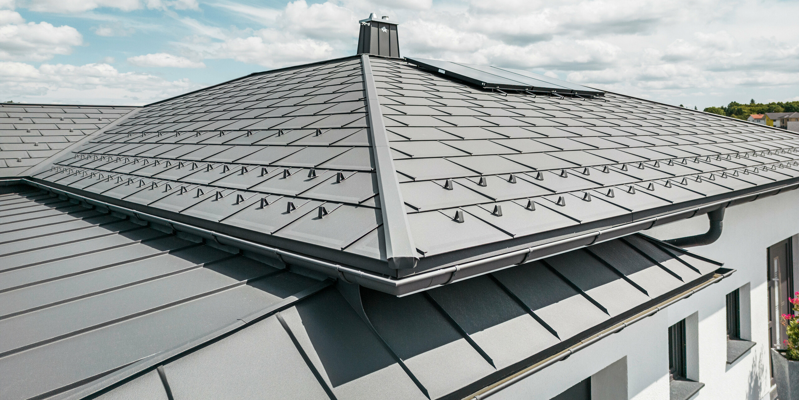 Strešný panel PREFA R.16 a PREFALZ ako aj dažďový zvod a polkruhový žľab P.10 tmavošedá na streche bungalovu