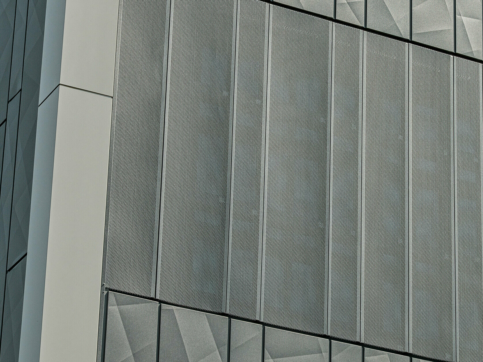 Pohľad na fasádu obchodu Eurospar v Rohrbachu s obkladom PREFA Siding.X a perforovanými obkladmi v antracitovej farbe. Prvky Siding.X vytvárajú živý geometrický vzor škár, zatiaľ čo perforované obklady ponúkajú modernú štruktúru priepustnú pre vzduch.