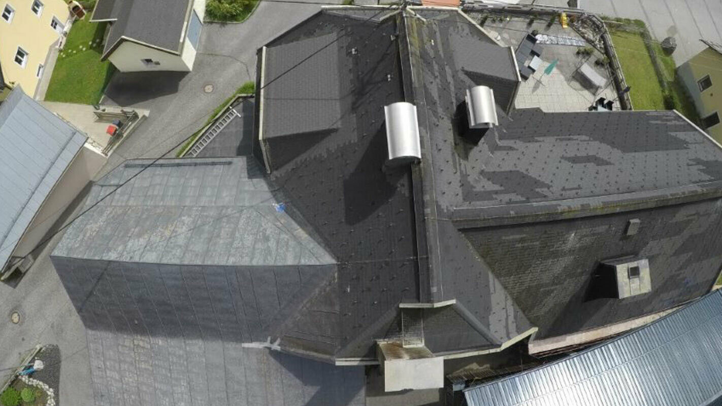 Pohľad z vtáčej perspektívy na starú strechu s mnohými detailami - úžľabiami, vikiermi a komínmi. Stará strešná krytina bola niekoľkokrát opravovaná a je škvrnitá.