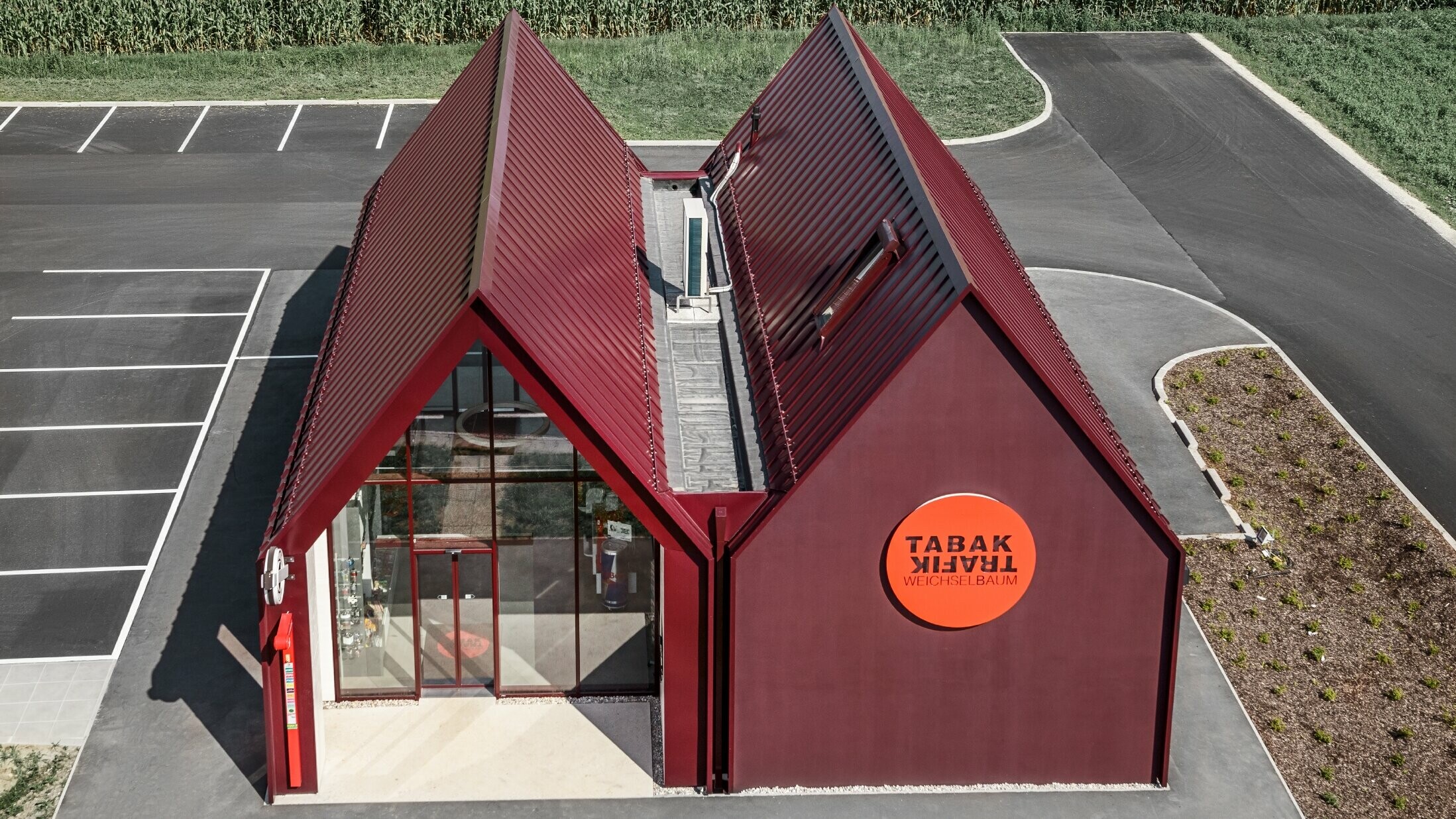 Moderná predajňa tabaku so sedlovou strechou s priamym prechodom na fasádu, s hliníkovým plášťom na dvojitú stojatú a uhlovú stojatú drážku v PREFA špeciálnej farbe čiernočervená